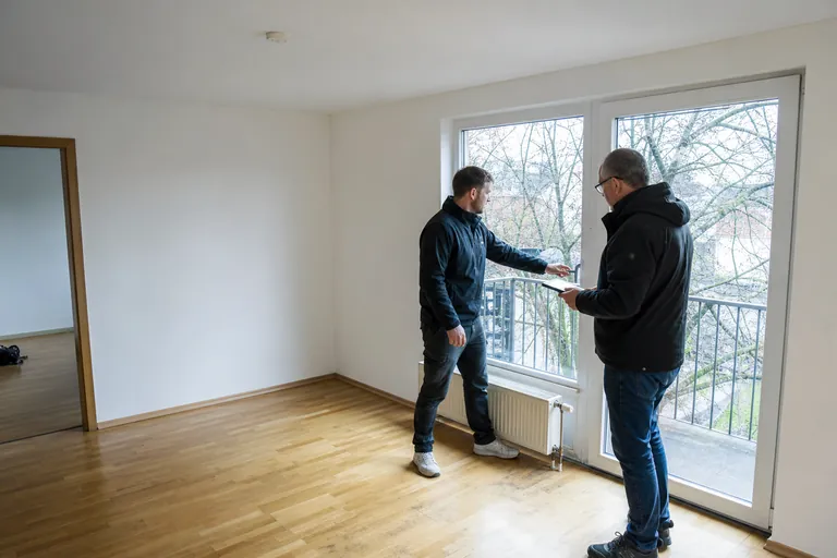 Vermieter und Mieter prüfen bei der Auszugsübergabe gemeinsam eine Balkontür.