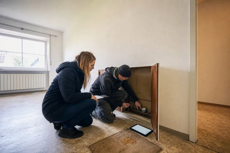 Zwei Personen lesen bei einer Wohnungsübergabe einen Wasserzähler ab.
